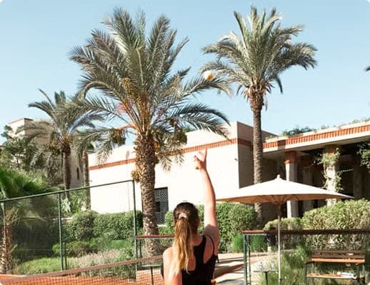 Woman tossing a tennis ball in front of palm trees