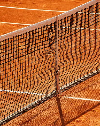 Net on a clay tennis court in morning sunlight